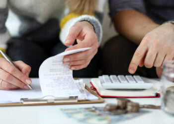 Close-up view of man and woman making account of family income. Writing down and calculating expenses. Attentive review of finance. Calculator on desk. Economy concept