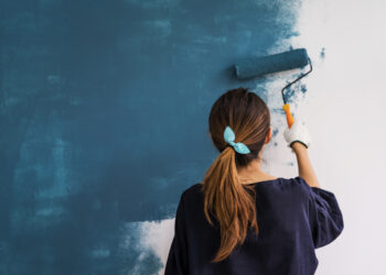 Young asian happy woman painting interior wall with paint roller in new house