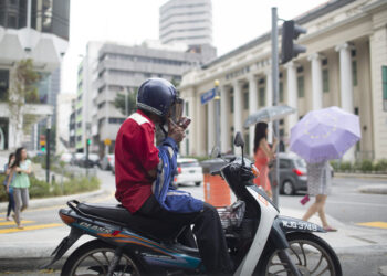 A man on a motorbike lights a cigarette on a street in Kuala Lumpur, Malaysia, on Tuesday, July 22, 2014. Photographer: Brent Lewin/Bloomberg
