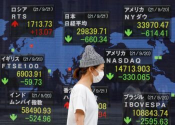 FILE PHOTO: A woman wearing a protective mask, amid the COVID-19 outbreak, walks past an electronic board displaying Japan and other countries' stock indexes outside a brokerage in Tokyo, Japan, September 21, 2021. REUTERS/Kim Kyung-Hoon