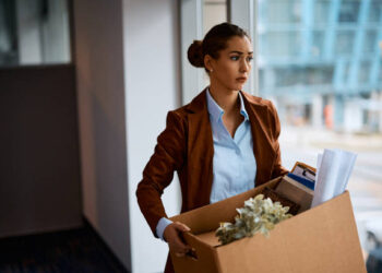Sad businesswoman with box of her belongings leaving the office after being fired from her job.