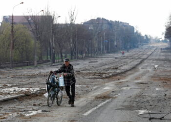 A local resident walks with a bicycle along a street near the Illich Steel and Iron Works during Ukraine-Russia conflict in the southern port city of Mariupol, Ukraine April 15, 2022. REUTERS/Alexander Ermochenko