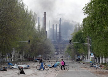 People walk their bikes across the street as smoke rises above a plant of Azovstal Iron and Steel Works during Ukraine-Russia conflict in the southern port city of Mariupol, Ukraine May 2, 2022. REUTERS/Alexander Ermochenko     TPX IMAGES OF THE DAY